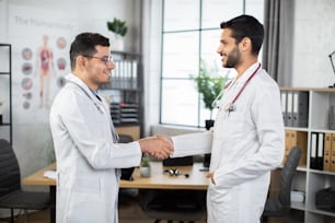 Good job, well done. Healthcare and professional work concept, where two smiling skilled Arab doctors at the clinic giving a handshake to each other, celebrating success and agreement.