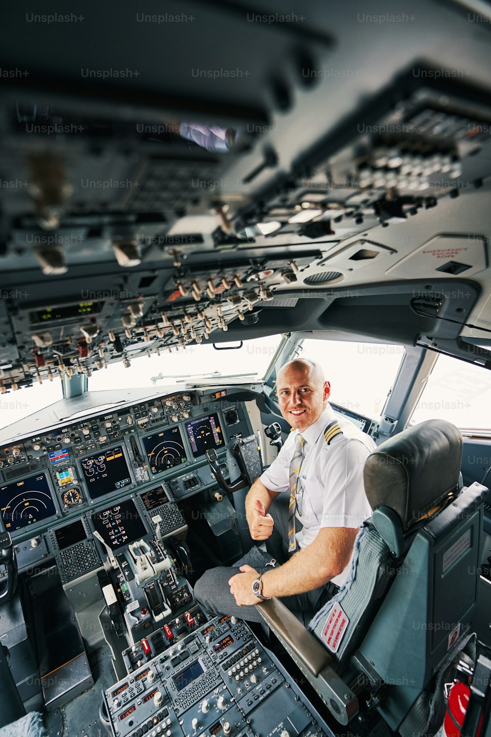 Lächelnd erfreut junger gutaussehender Flugkapitän in Uniform, der ein Daumen-hoch-Zeichen aus seinem Cockpit macht