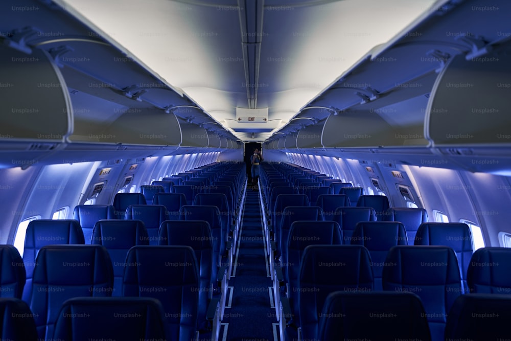 Interior de un avión con una azafata de pelo oscuro, esbelta y elegante con un polvorín de pie en el pasillo de la cabina de pasajeros