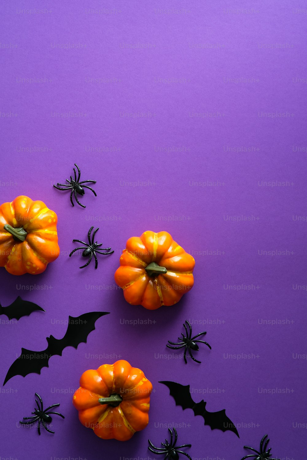 Happy Halloween holiday concept. Halloween decorations, pumpkins, bats on purple background. Halloween party greeting card mockup with copy space. Flat lay, top view, overhead.