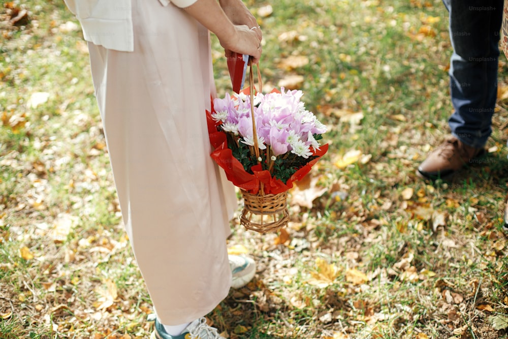 Stylish  woman in modern outfit holding basket of flowers and sweets after family congratulations.Close up. Celebrating birthday with family and friends at picnic party outdoor