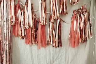 Stilvolle rosa Girlande hängt im Zimmer. Moderne Roségold-Quastengirlande auf beigefarbenem Stoff im modernen Raum für Geburtstagsfeier. Party-Dekor