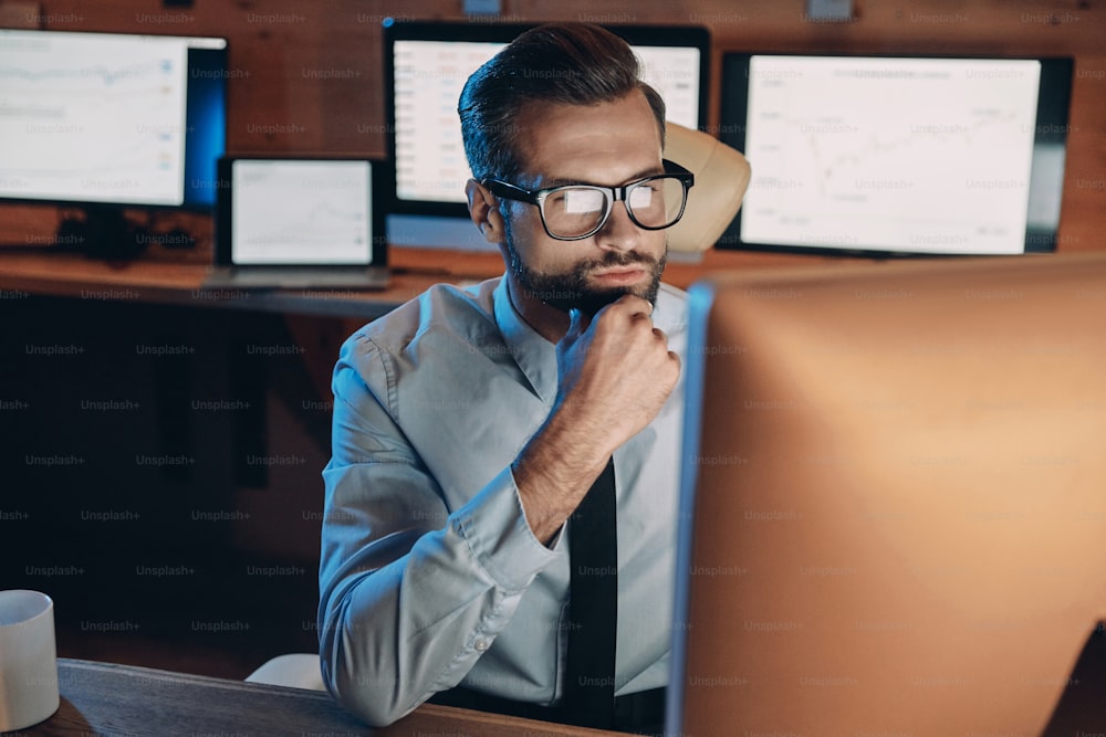 Jeune homme confiant travaillant sur un ordinateur tout en restant tard au bureau