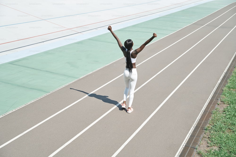 Vista dall'alto di bella giovane donna africana in abbigliamento sportivo che tiene le braccia alzate mentre si trova sulla pista da corsa all'aperto
