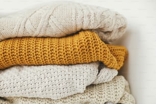 Cozy knitted sweater background. Pile of white, yellow and beige knit sweaters close up. Hello autumn. Stylish wardrobe for cold season