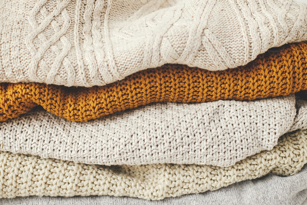 아늑한 니트 스웨터 배경. 흰색, 노란색, 베이지색 니트 스웨터 더미가 닫힙니다. 안녕하세요 가을입니다. 추운 계절을위한 세련된 옷장