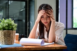 Stressed woman holding her head and reading financial reports.