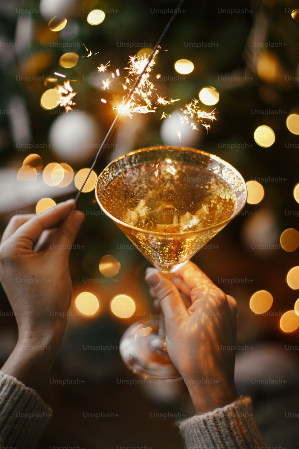 Feliz Ano Novo! Mulher que celebra com luz de fogo-de-artifício e taça de champanhe no fundo da árvore de Natal e estrela brilhante. Mãos segurando espumante ardente e bebida. Momento atmosférico