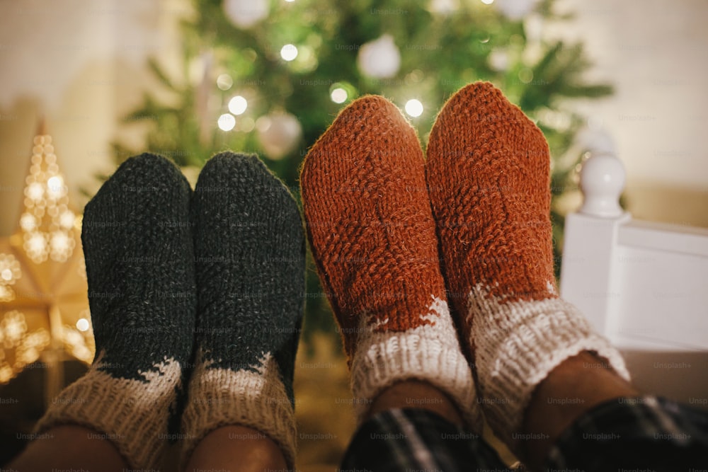 Couples pieds dans des chaussettes en laine douillettes sur fond d’arbre de Noël en lumières dans la salle de soirée festive. Célébrer les vacances d’hiver ensemble, des moments agréables en famille à la maison. Chaussettes chaudes et élégantes