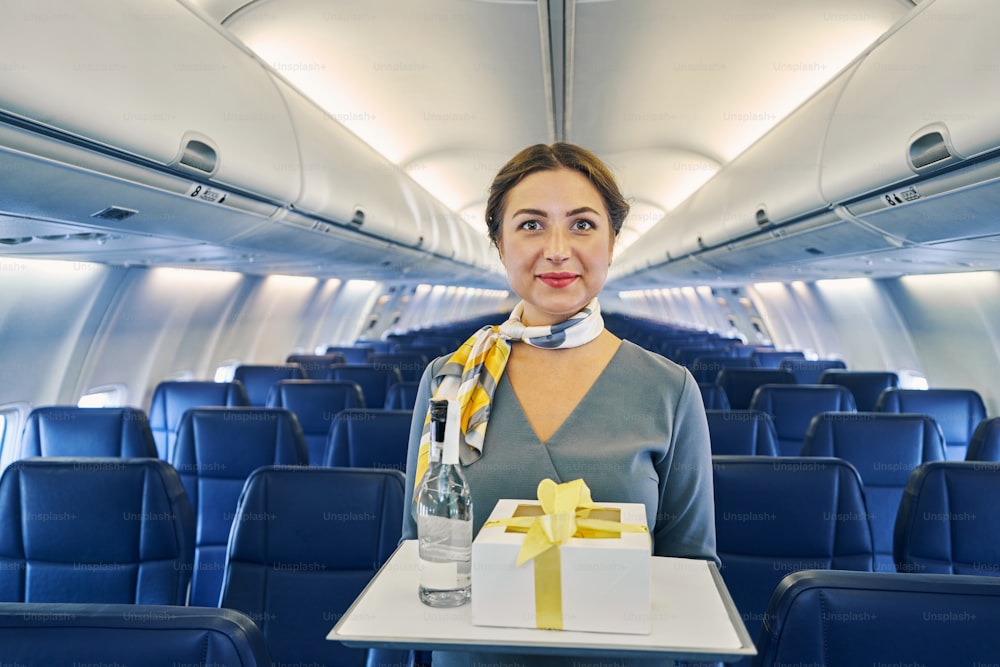 Ritratto in su di una bella hostess di volo che trasporta una confezione regalo e una bottiglia di bevanda per i passeggeri