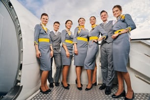 Two handsome elegant stewards and five beautiful stylish young stewardesses posing for the camera outdoors