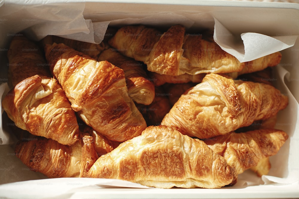 Delicious croissants on parchment in basket on sunny picnic outdoors. Top view on freshly baked croissants in warm sunshine. Tasty bread and snack on party or picnic. Authentic image