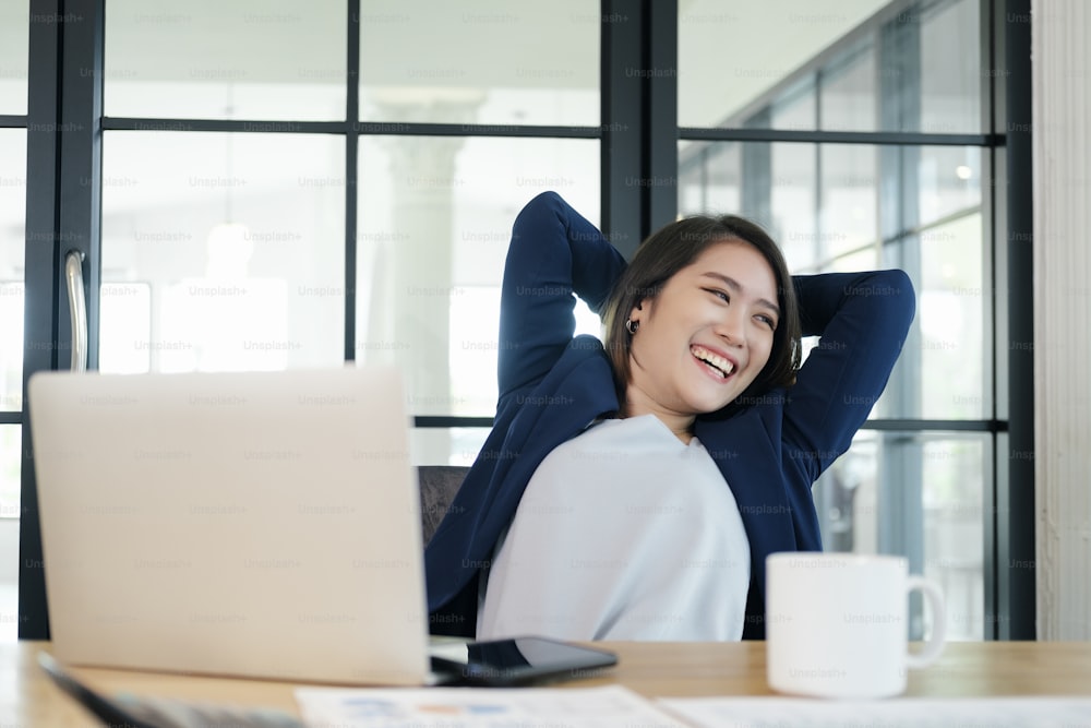 Mujer de negocios sonriente tranquila que se relaja en la silla de oficina cómoda con las manos detrás de la cabeza, mujer feliz que descansa en la oficina satisfecha después del trabajo hecho