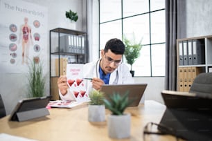 Online appointment, healthcare concept. Male Arab doctor using wireless laptop for online video call with colleague or patient, explaining liver cancer desease symtopms and stages