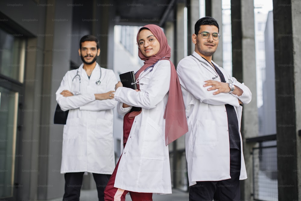 Asian Indian medical team standing in row and looking at the camera. Confident doctors team outdoor. Arab male and female doctors looking at camera and smiling while their colleague standing in behind
