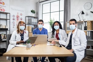 Pandemic outbreak. Professional multiracial medical specialists using modern laptops and tablets during conference at hospital, discussing important new information about virus at boardroom.