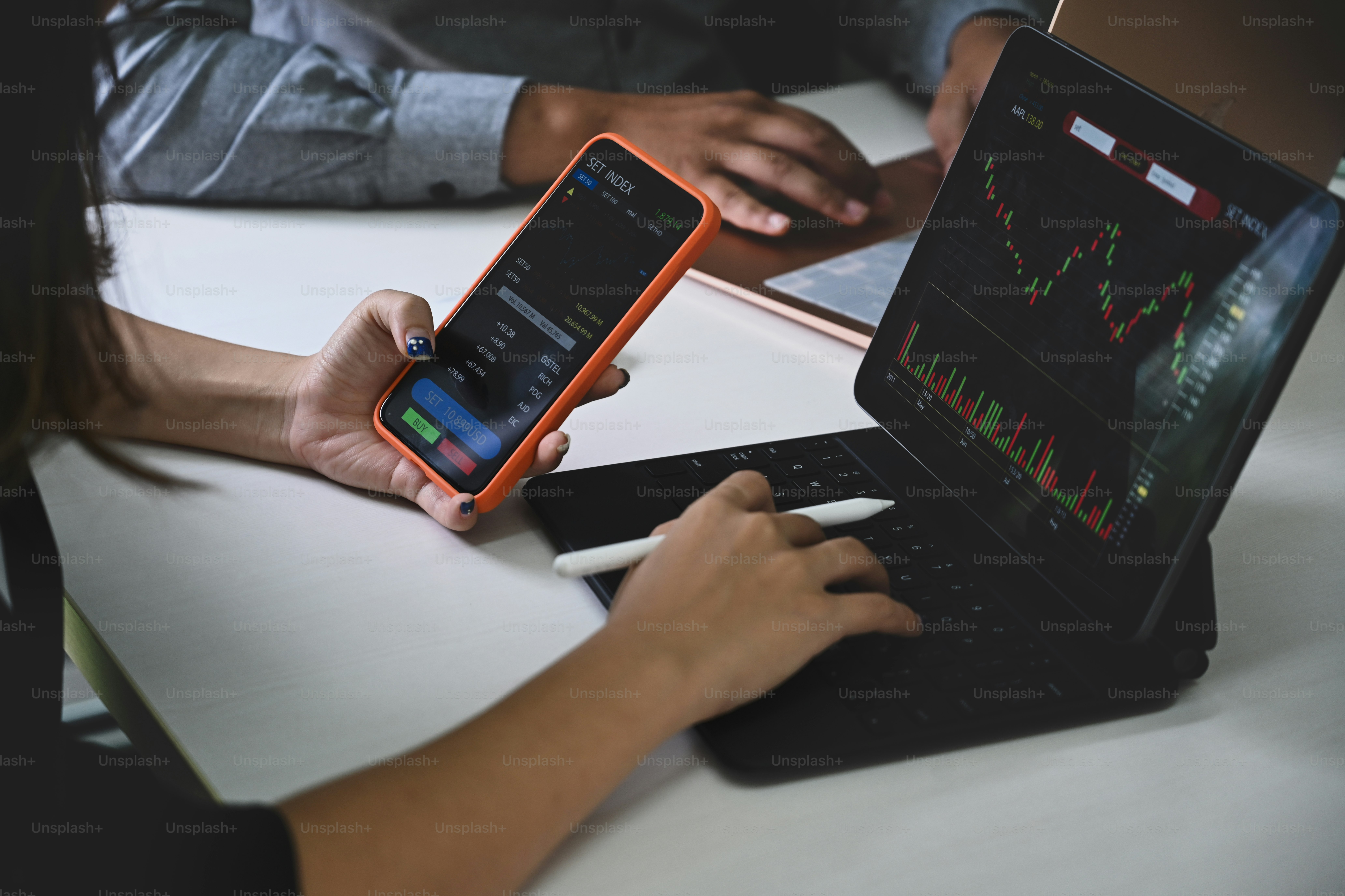 Businesswoman using smart phone and analyzing investment charts with computer tablet.