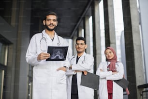 Asian Indian medical team standing in row and looking at the camera. Confident doctors team outdoor. Arabic male doctor looking at camera and smiling while his colleagues standing in a row behind