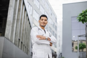 Portrait d’un jeune médecin arabe asiatique confiant debout à l’extérieur du bâtiment de l’hôpital avec les bras croisés et le stéthoscope autour du cou. Portrait d’un professionnel de la santé