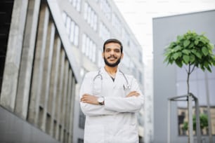 Portrait d’un jeune médecin ou d’un étudiant arabe asiatique en uniforme médical avec stéthoscope sur le campus universitaire moderne des bâtiments de l’hôpital en arrière-plan