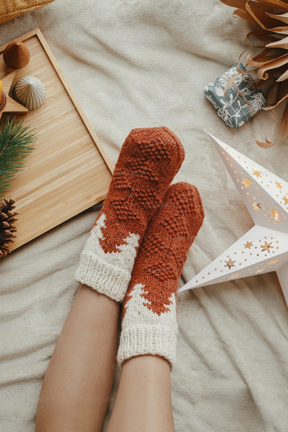 Woman legs in warm socks on soft blanket with christmas star, trees and candle, top view. Cozy moments at home. Winter and autumn holidays.