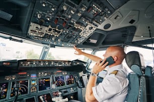 Side view of a professional Caucasian male pilot with his smartphone looking at the dashboard