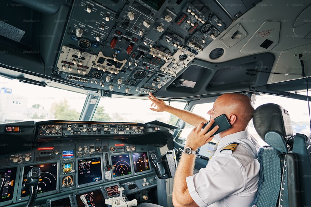 Seitenansicht eines professionellen kaukasischen männlichen Piloten mit seinem Smartphone auf das Armaturenbrett