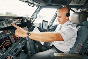 Serious male pilot with a pre-flight checklist in his hand sitting alone in the cockpit