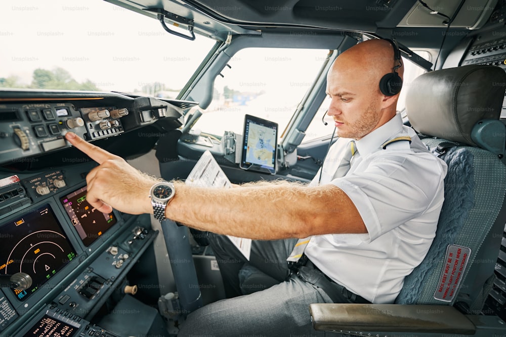 Ernsthafter männlicher Pilot mit einer Checkliste vor dem Flug in der Hand, der allein im Cockpit sitzt