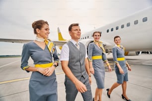 Smiling beautiful elegant female flight attendants and their attractive male colleague going along the runway