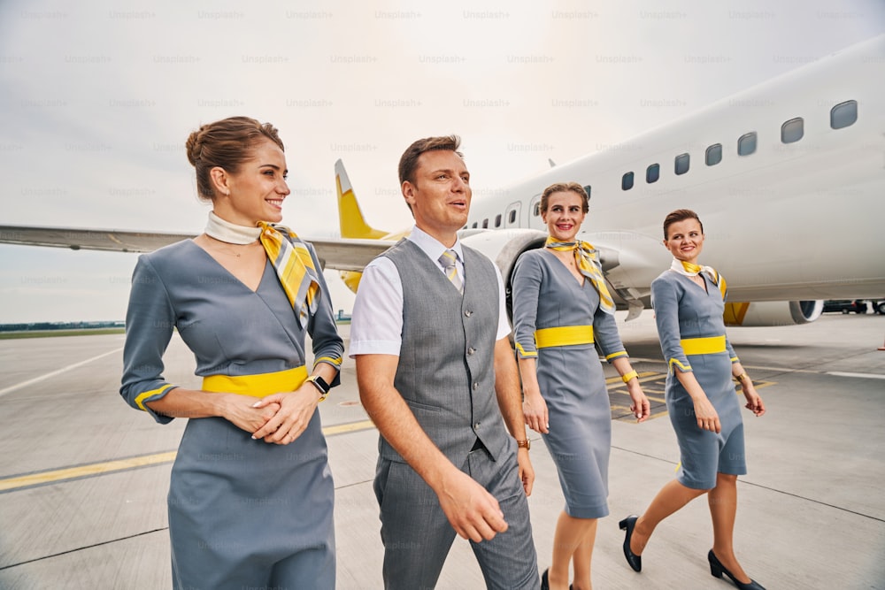 Smiling beautiful elegant female flight attendants and their attractive male colleague going along the runway