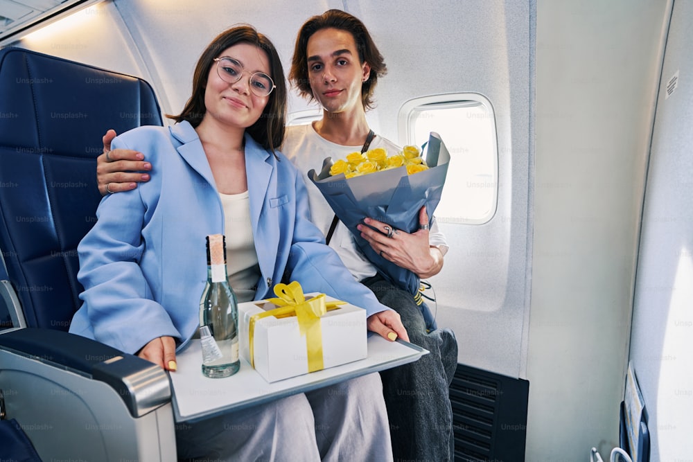 Cute tranquil young man and his smiling beautiful dark-haired girlfriend in eyeglasses sitting in the first class cabin