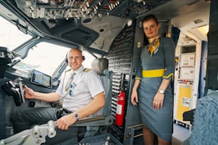 Attractive young Caucasian air hostess standing by a contented airline captain in the flight deck