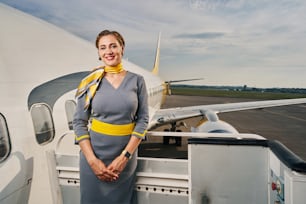 Front view of a smiling stewardess leaned against the handrail of the boarding stairs looking ahead