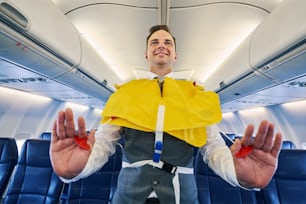 Low angle of a cute experienced professional flight attendant pulling downward on the cords of his life vest