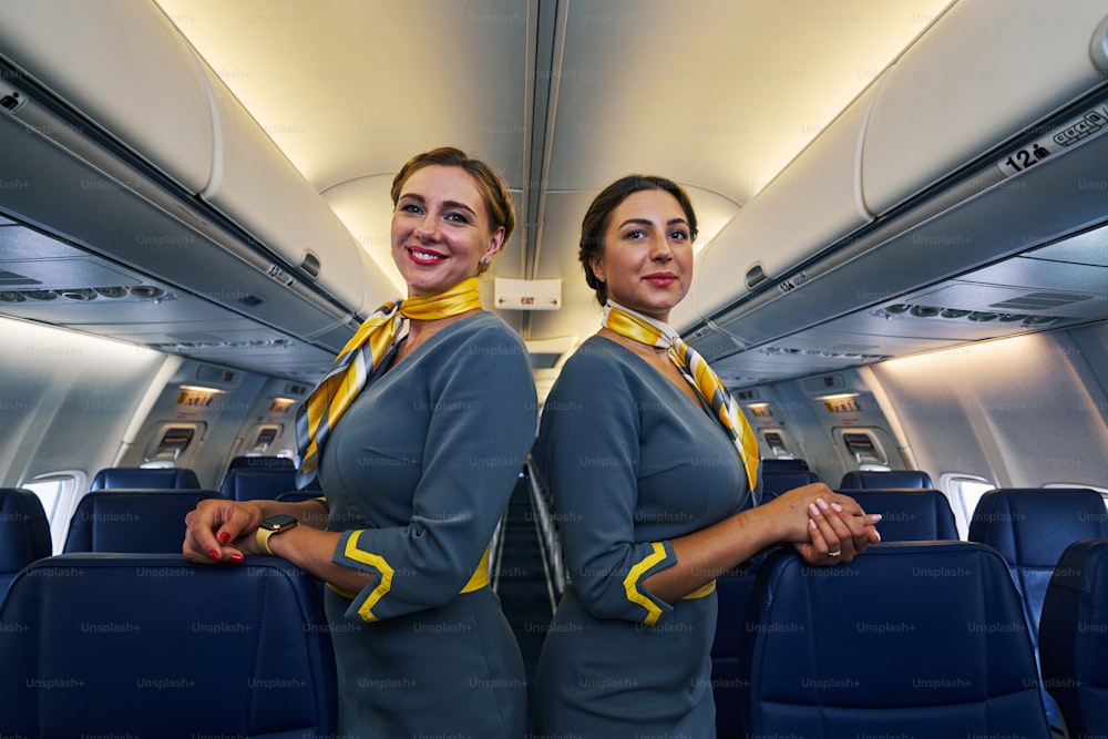 Two beautiful Caucasian elegant professional female flight attendants in uniforms standing in the cabin aisle