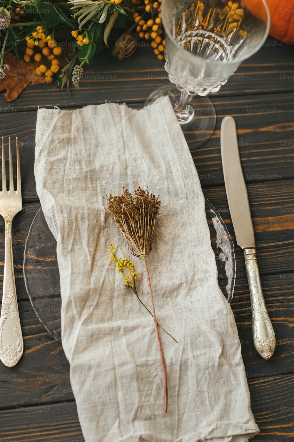 ヴィンテージのカトラリー、リネンナプキン、カボチャと秋の花のアレンジメントが置かれた木製のテーブルにハーブが置かれたモダンなプレート。農家の素朴な秋の結婚式。環境にやさしい感謝祭のディナーテーブルセッティング