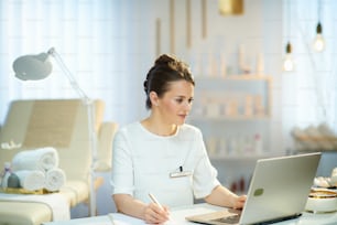 middle aged woman employee with laptop in modern beauty studio.