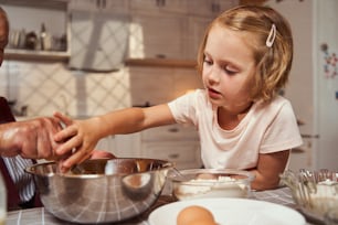 Une personne à l’extérieur de la photo saisit le fouet d’un enfant tout en mélangeant des ingrédients dans un bol sur la table.