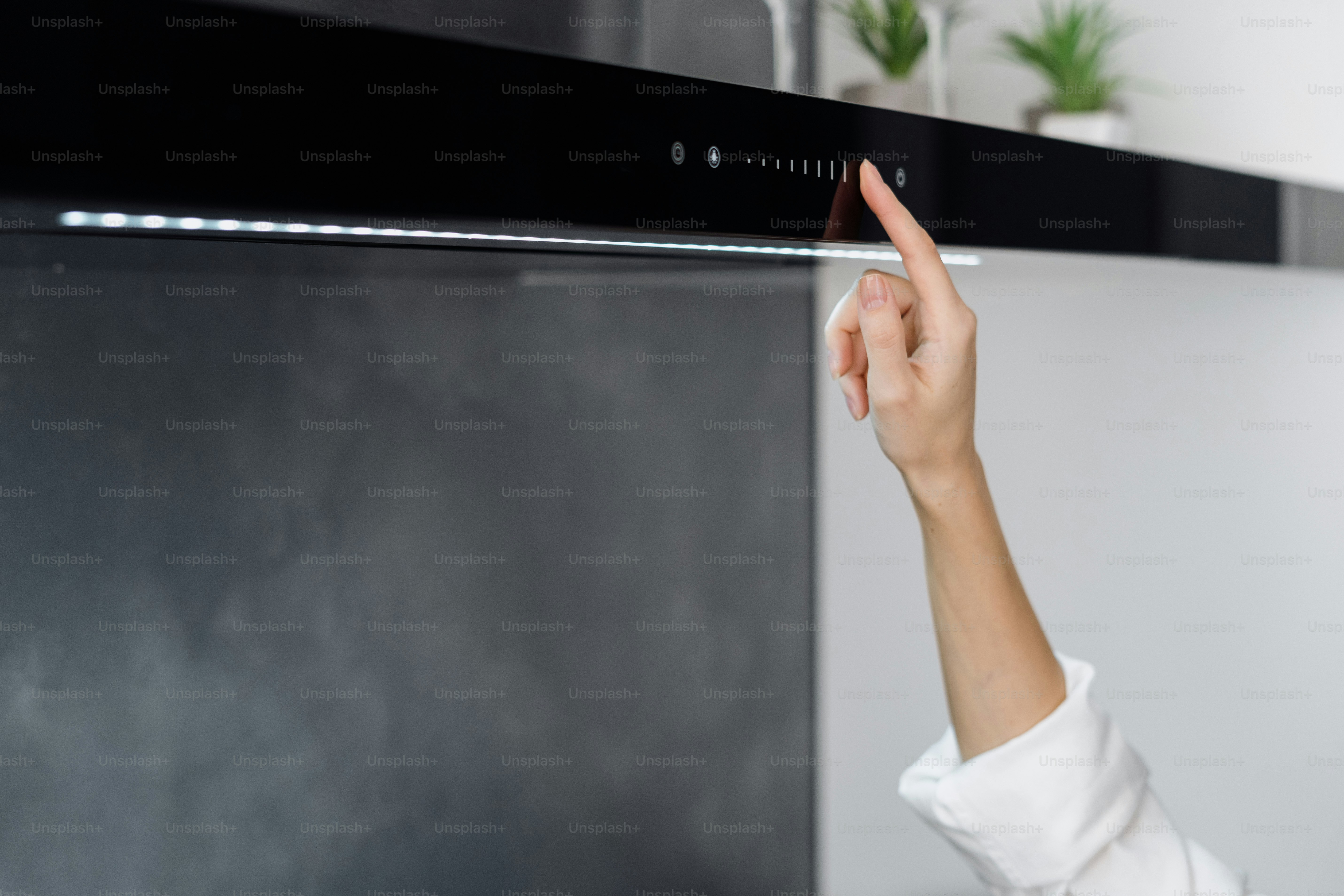 Plan recadré d’une femme ajustant la hotte aspirante ou l’échappement tout en cuisinant dans une cuisine minimaliste entièrement meublée avec des appareils modernes intégrés
