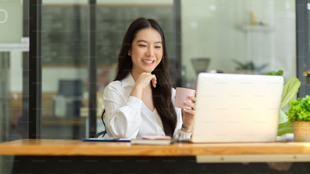 Happy businesswoman having online meeting, video conference with her team. sitting at office, holding coffee cup