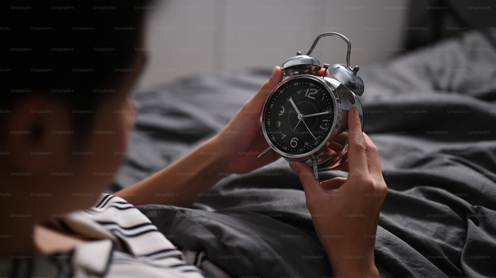 Young man sitting in bed and turning off an alarm clock.