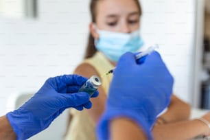 Arzt impft Mädchen. Injektion von COVID-19-Impfstoff in den Arm des Patienten. Kleinkind mit Gesichtsmaske wird geimpft, Coronavirus, Covid-19 und Impfkonzept.