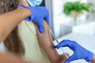 Medico che vaccina la ragazza. Iniezione di vaccino COVID-19 nel braccio del paziente. Ragazza con maschere mediche che viene vaccinata contro il covid-19, medico che fa l'iniezione di vaccino contro il coronavirus in ospedale.