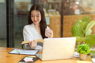 Attractive businesswoman reading book, sitting at coffee shop, relaxed female entrepreneur