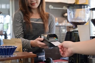 Female waiter holding credit card swipe machine while customer making payment in coffee shop with credit card.