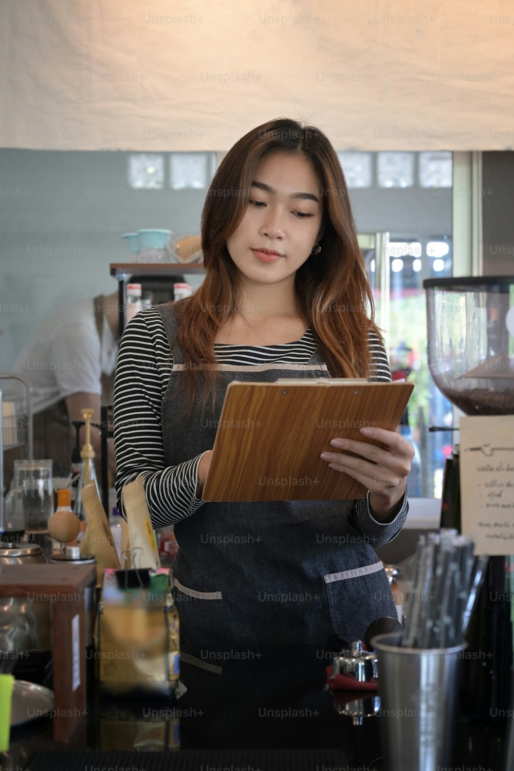 Portrait of young female waitress in apron standing in modern coffee shop.