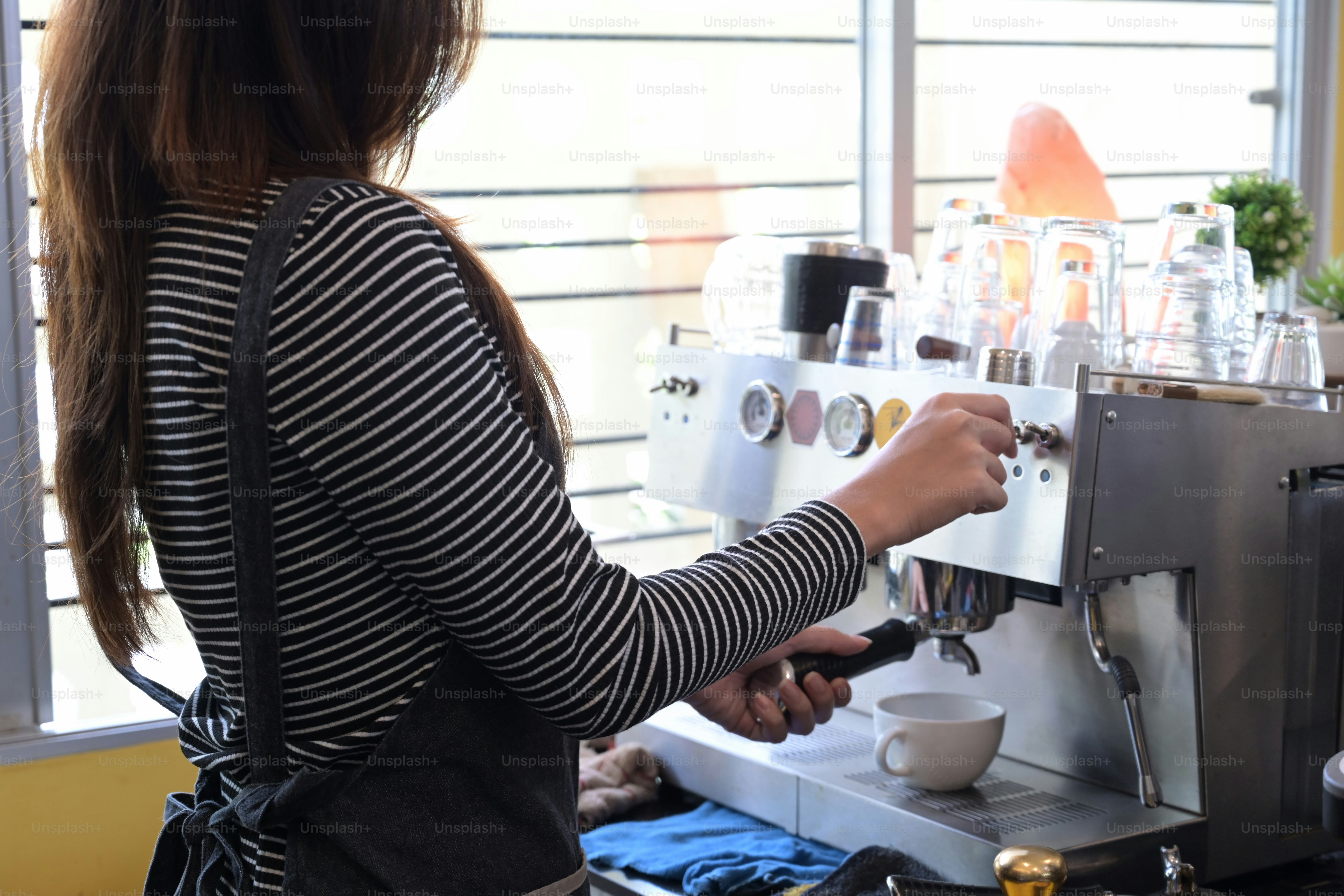 Side view of barista preparing coffee with coffee machine in modern cafe.