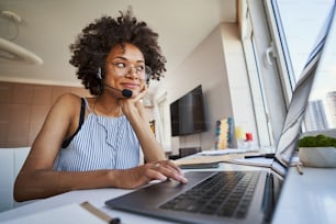 Retrato de una trabajadora remota satisfecha con el auricular y las gafas sentada en la computadora portátil