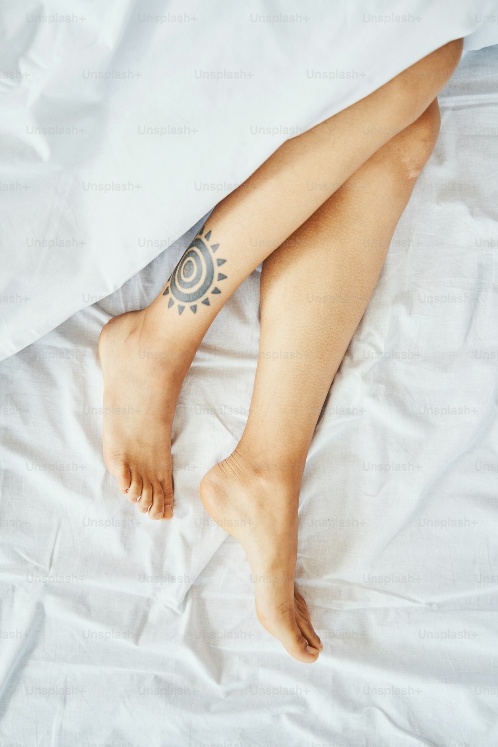 Cropped photo of a woman with two beautiful slim shaved legs lying on the white sheet covered with the blanket